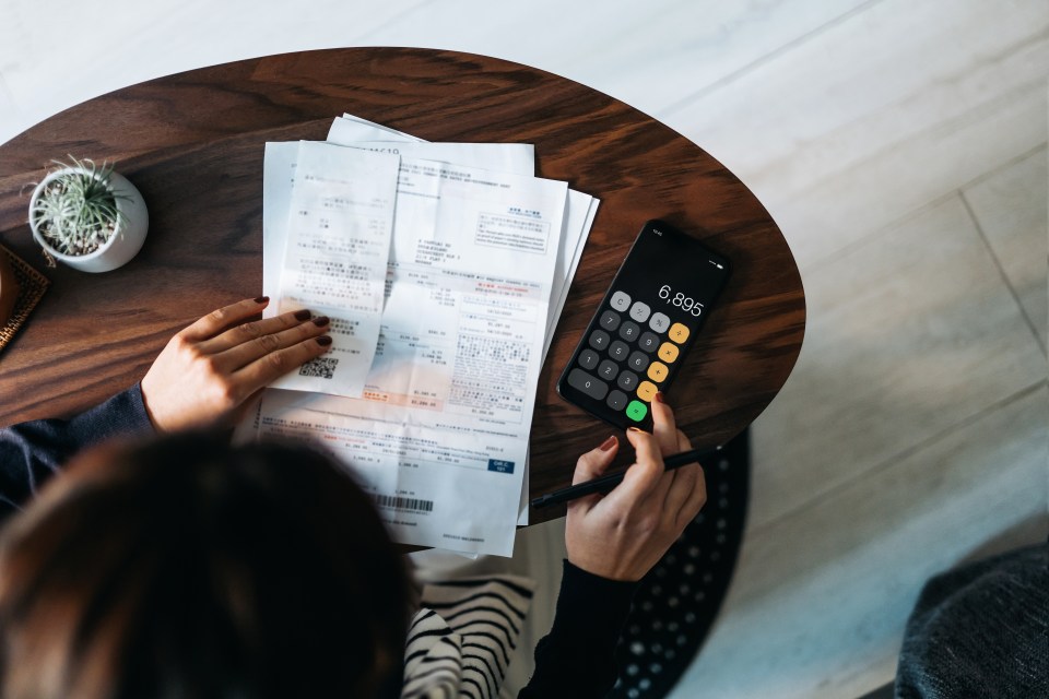 Woman reviewing bills and using calculator app on phone.