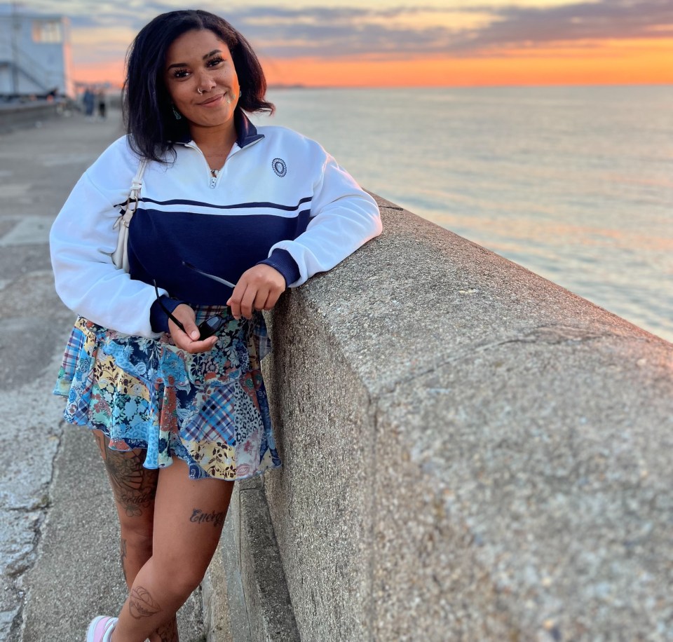 Woman standing by ocean at sunset.