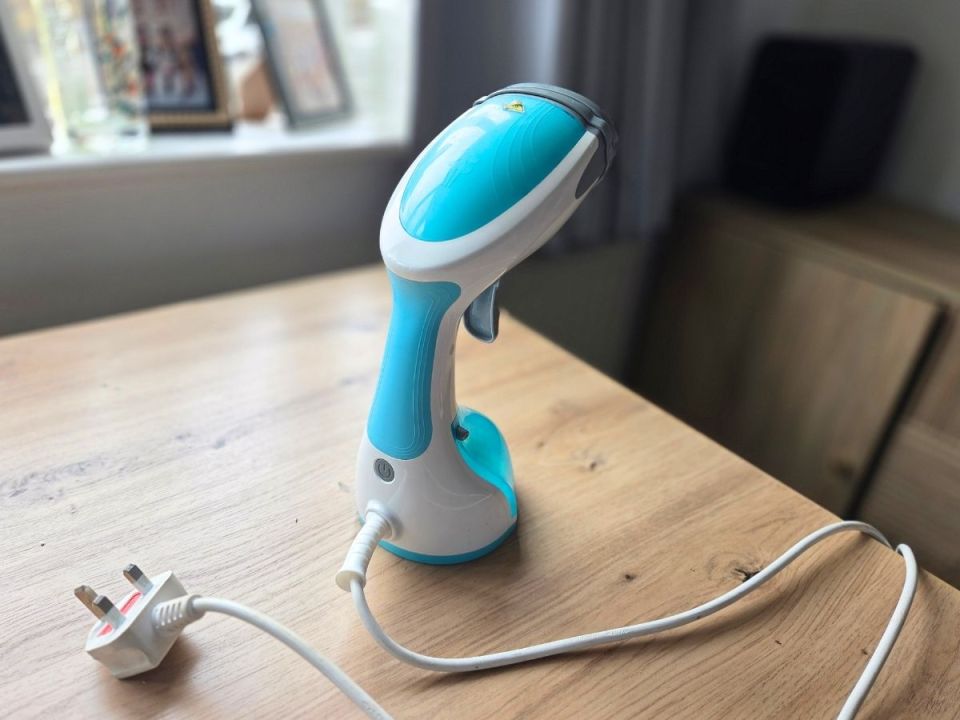 A blue and white handheld garment steamer on a wooden table.