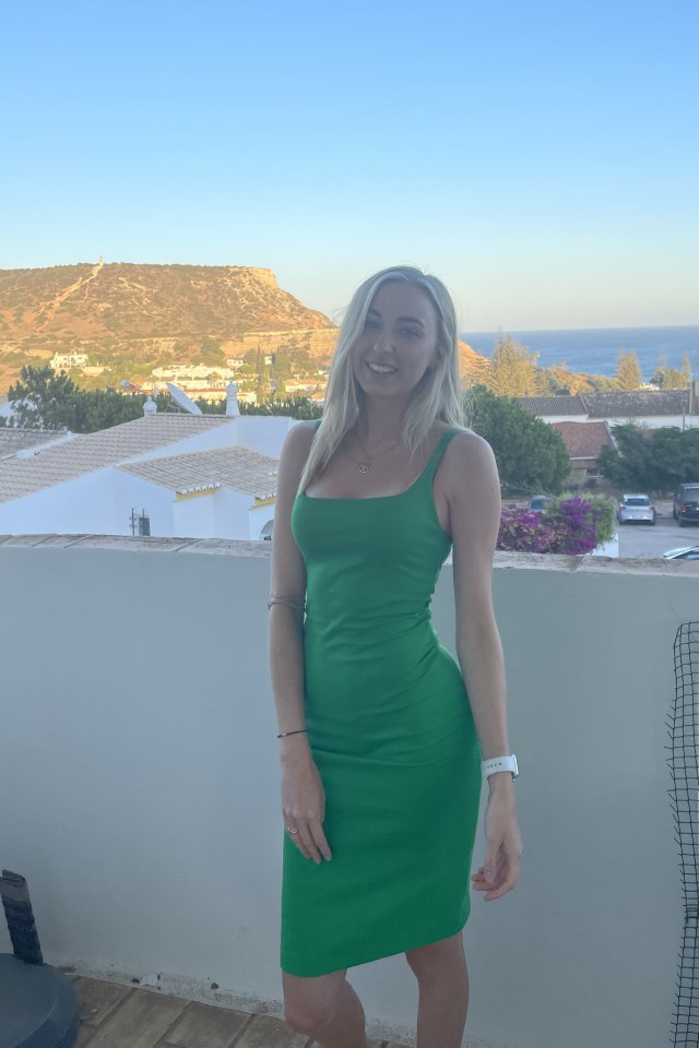 Woman in green dress on balcony overlooking ocean and hills.