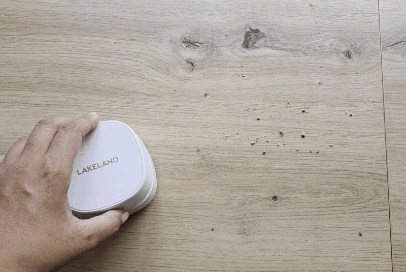 Hand holding a Lakeland cleaning device on a wooden surface.