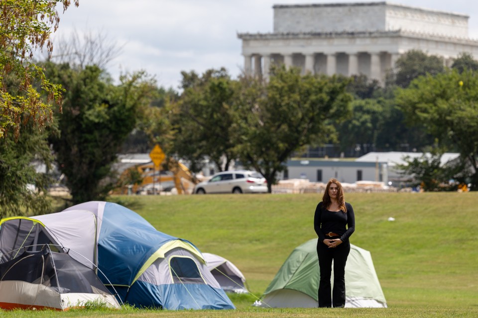 Woman stands in front of tents with the Lincoln Memorial in the background.