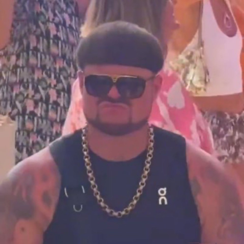 Man wearing sunglasses, a gold chain, and a black tank top.