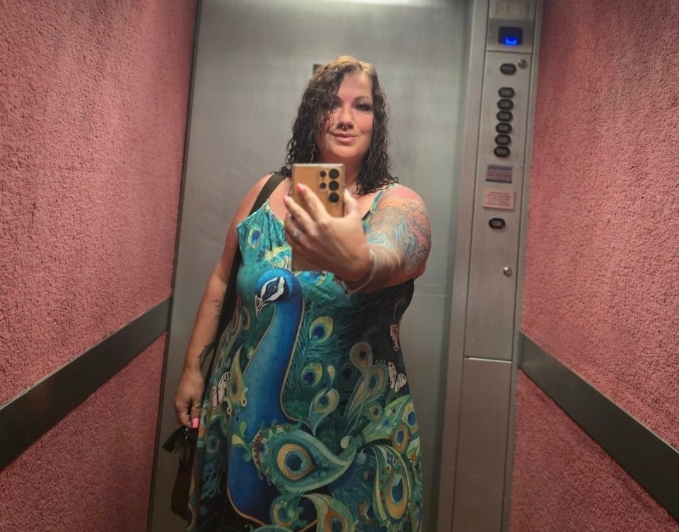 Woman in peacock dress taking a selfie in an elevator.