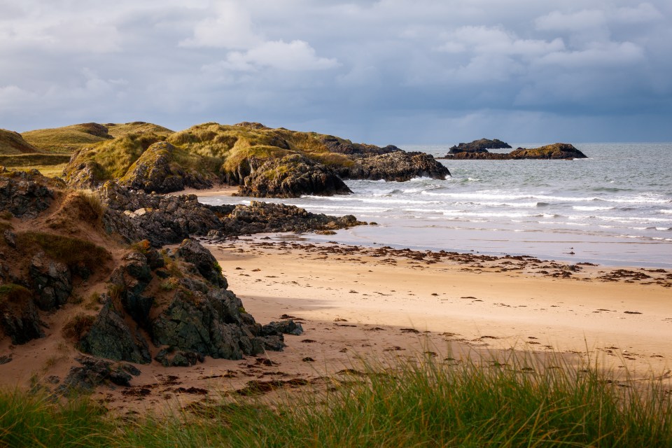 Sandy beach with rocky shoreline and ocean waves.