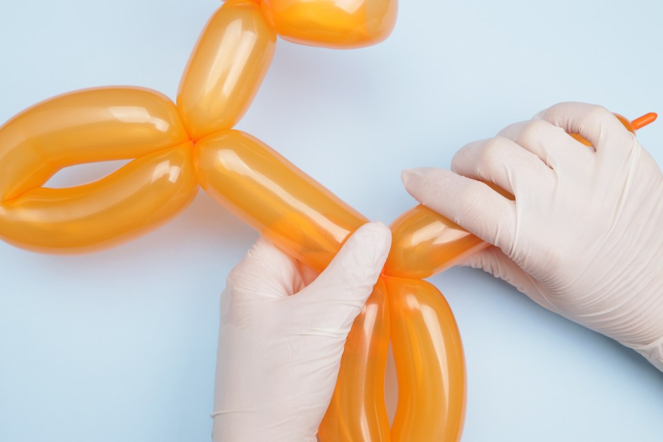 Hands in gloves twisting an orange balloon into a dog shape.