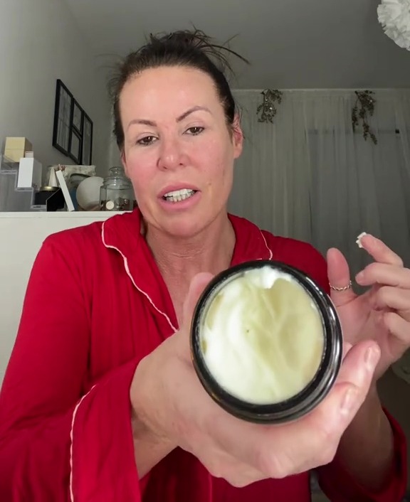 Woman in red pajamas holding up a jar of cream.