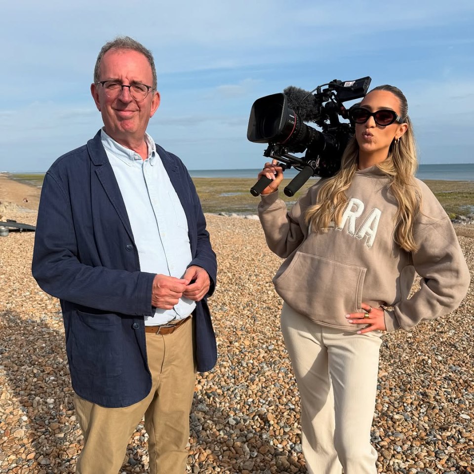 Two people on a beach; one holds a video camera.