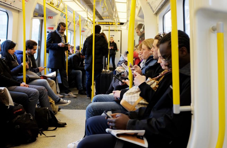 Commuters on a London Underground train using smartphones and electronic devices.