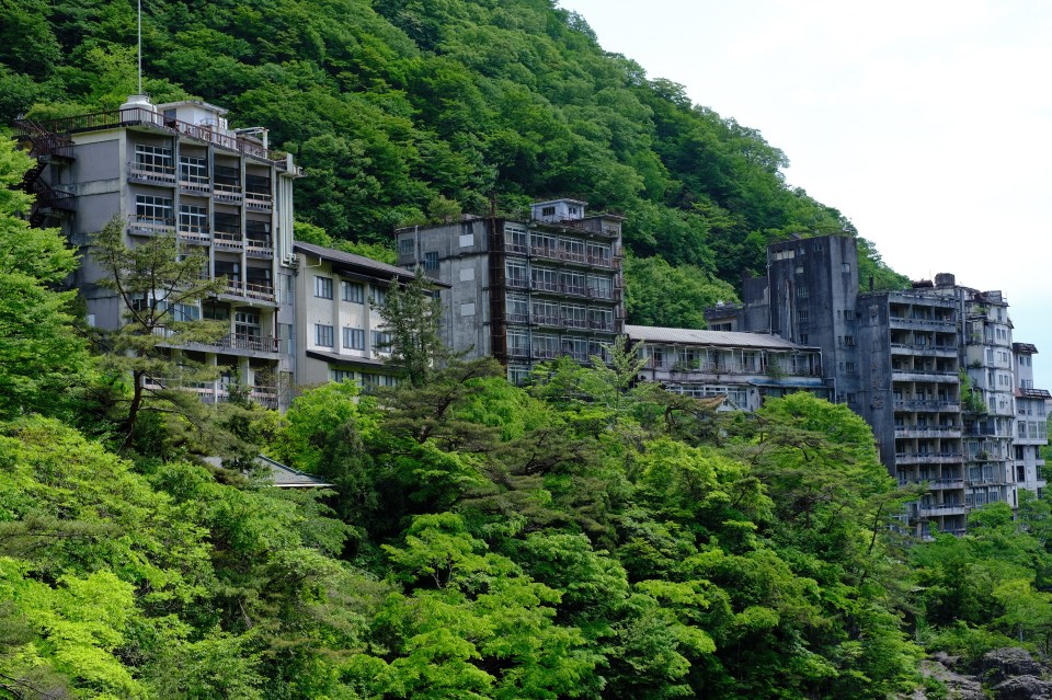Overgrown abandoned hotel buildings on a hillside.