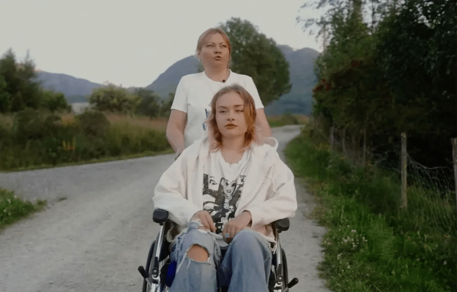 Woman pushing a young woman in a wheelchair down a country road.