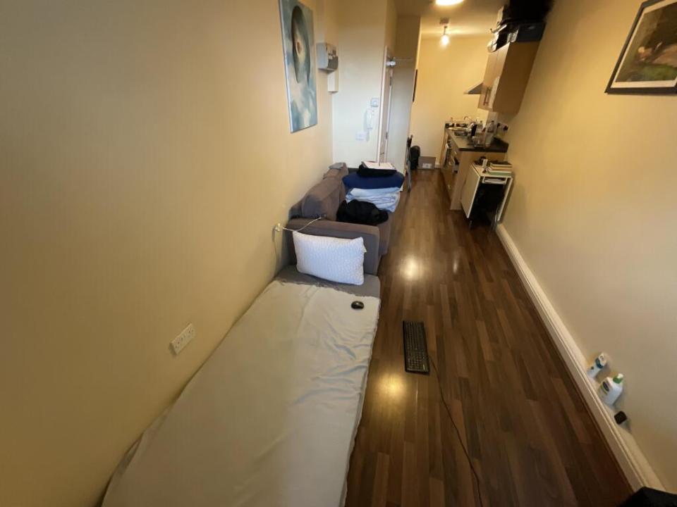 Narrow studio apartment with a bed, sofa, and small kitchen.