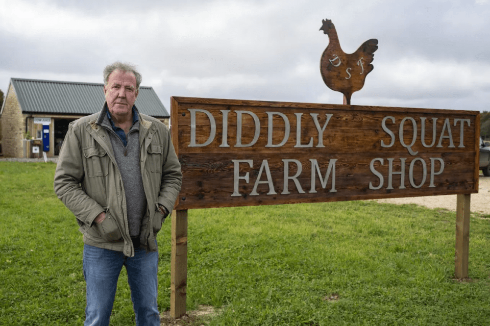 Jeremy Clarkson standing by the Diddly Squat Farm Shop sign.
