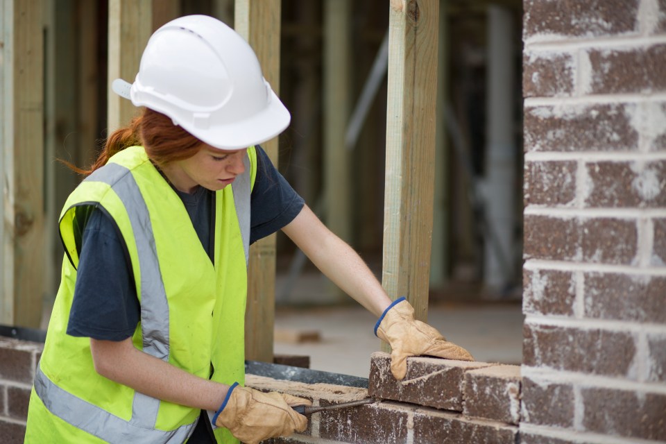 A young woman bricklayer working on a wall.