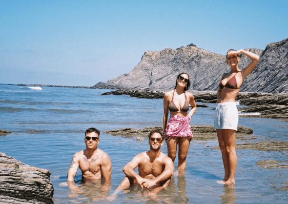 Four friends at the beach. Two men are in the water, and two women are standing in shallow water.