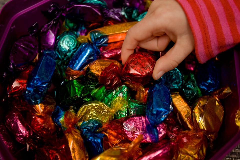 Child's hand selecting a chocolate from a box of colorful candies.