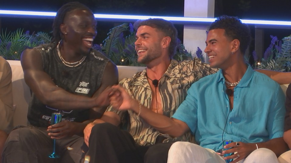 Three men laughing and holding hands on a couch.