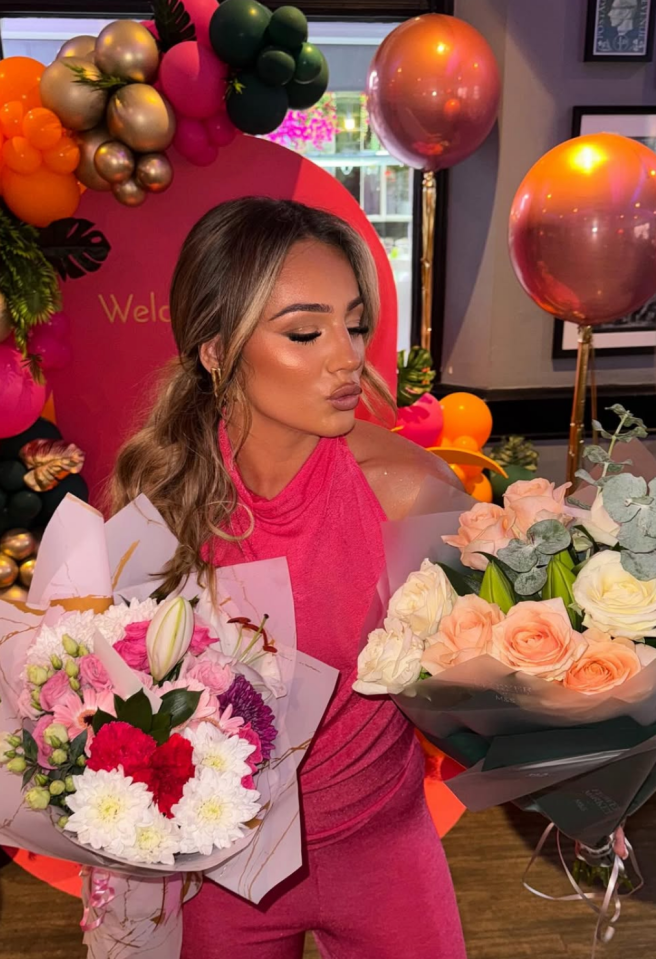 Woman in pink holding two bouquets of flowers.