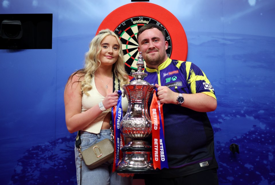 Luke Littler of England with the Phil Taylor Trophy and Faith Millar.