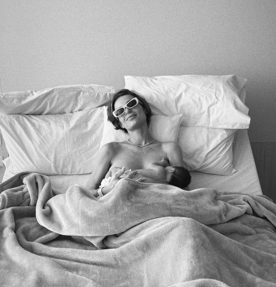 Black and white photo of a mother breastfeeding her newborn baby while wearing sunglasses in a hospital bed.