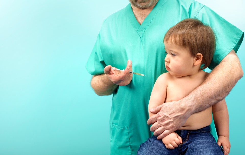 Doctor holding baby, preparing to give injection.