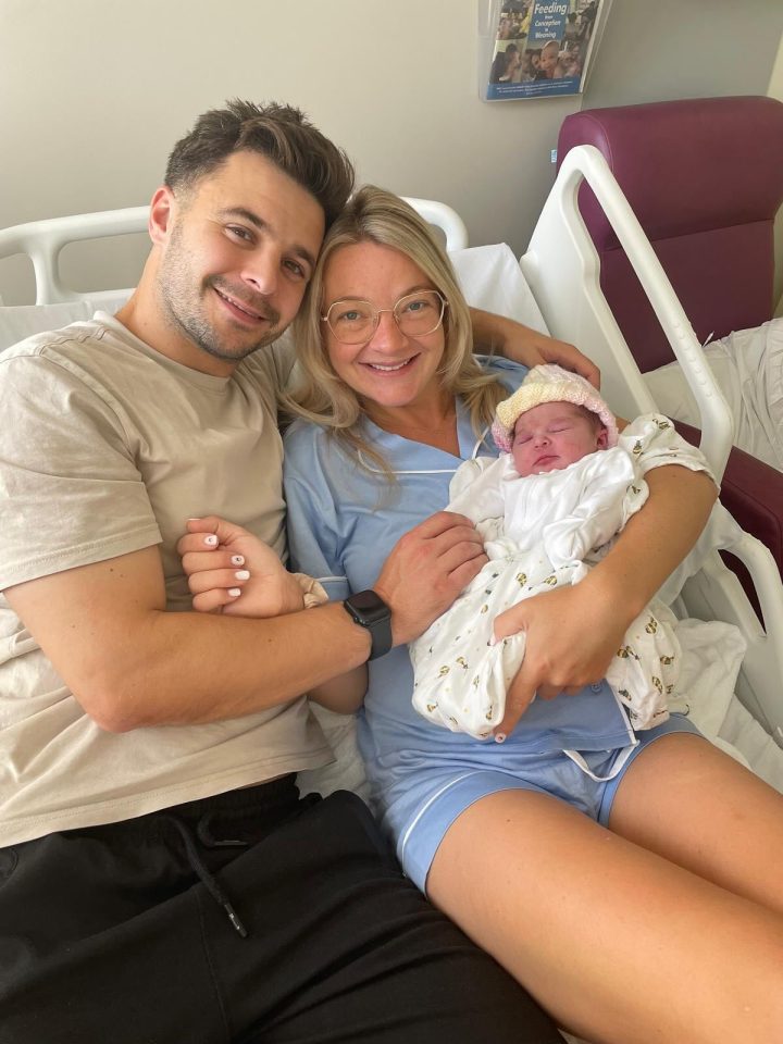 New parents holding their newborn baby in a hospital bed.