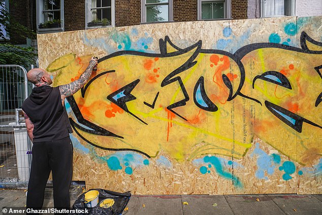 A street artist spray paints a boarded up property before the bank holiday weekend