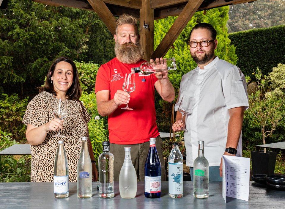 Three people pouring and holding glasses of water from a selection of bottled water.