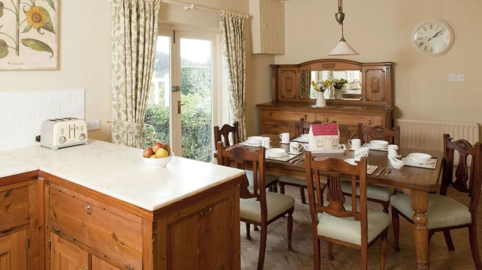 Kitchen and dining area in a cottage with wooden furniture and garden views.