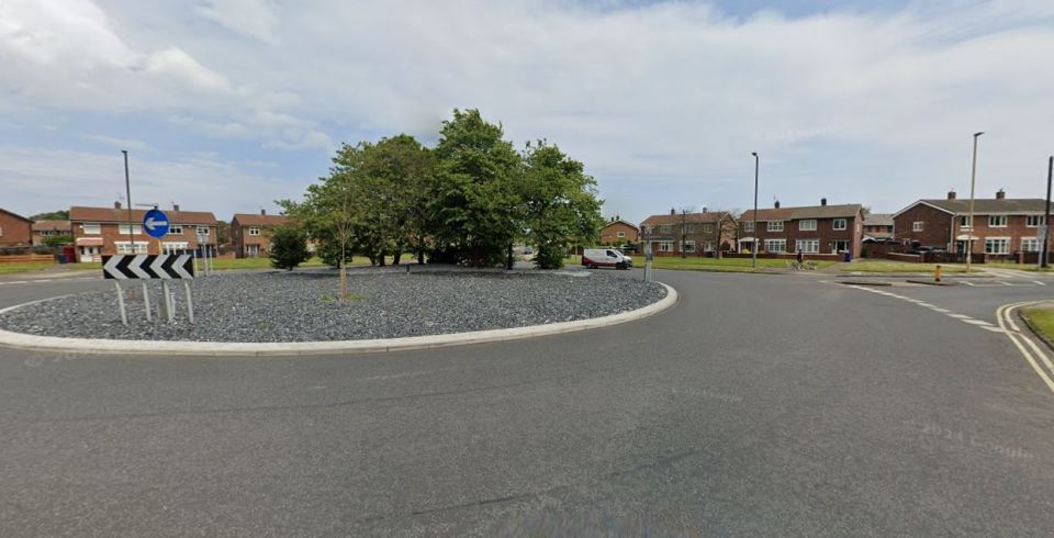 Residential roundabout with houses and a van.
