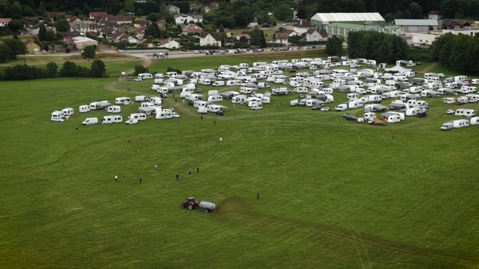 Aerial view of a tractor spreading manure near numerous RVs parked in a field.