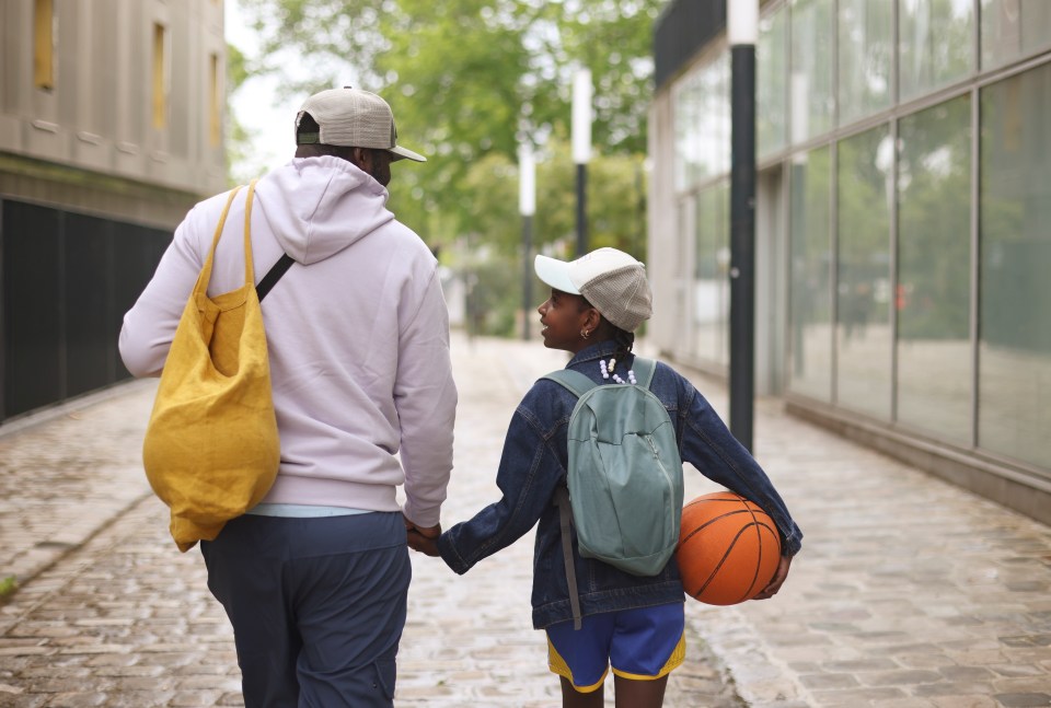 A father and daughter holding hands and walking to play basketball.