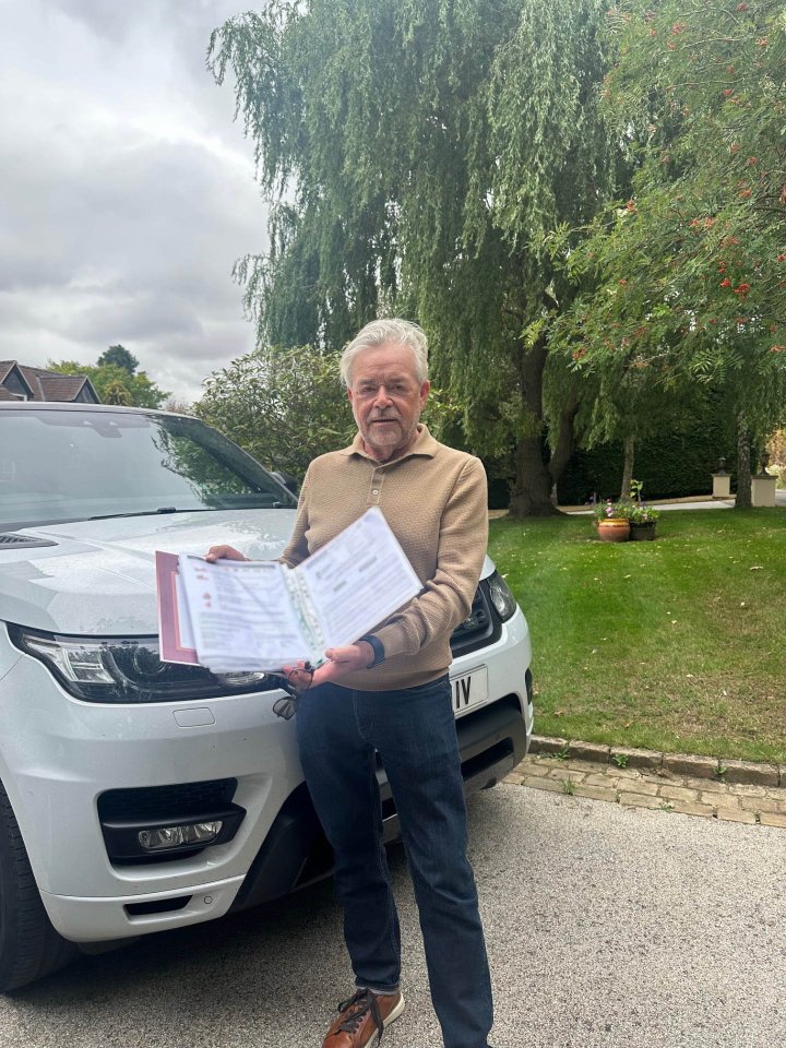 A man stands in front of his car holding a folder of paperwork related to a parking ticket dispute.