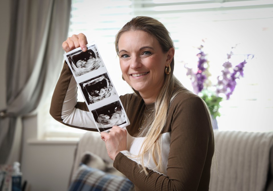 A pregnant woman holding up her baby scan photos.