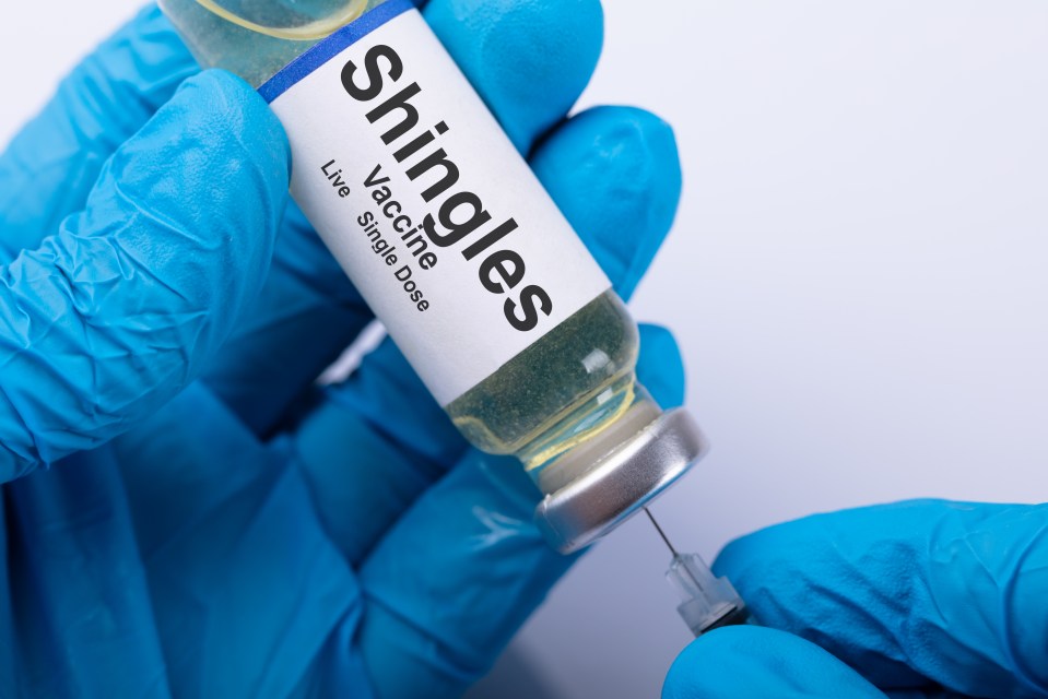 Close-up of gloved hands drawing shingles vaccine into a syringe.