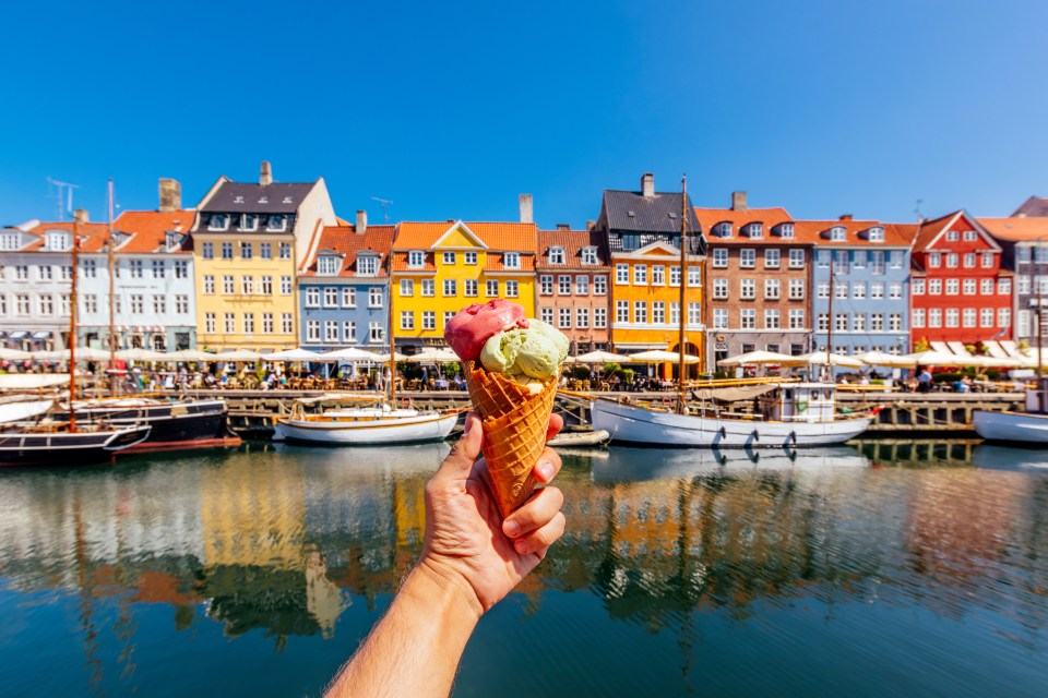 Hand holding ice cream cone in front of colorful buildings and canal.
