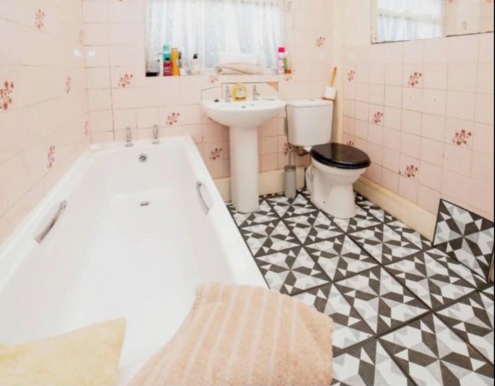 Photo of a bathroom with a pink tiled wall, a white bathtub, and patterned floor tiles; listed for £200,000.