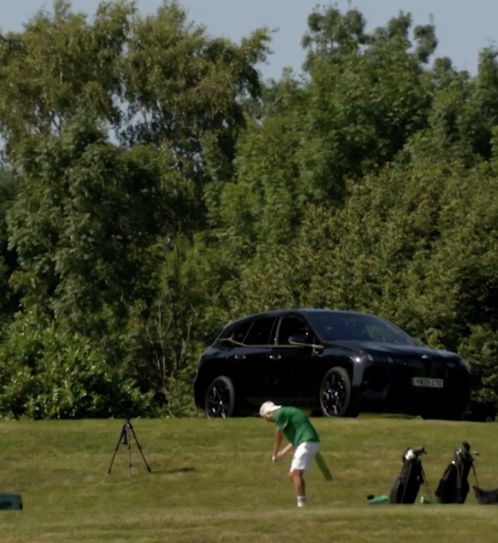 Golfer practicing on a golf course with a black SUV in the background.