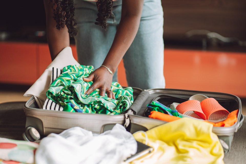 Person packing a suitcase with clothes and shoes.