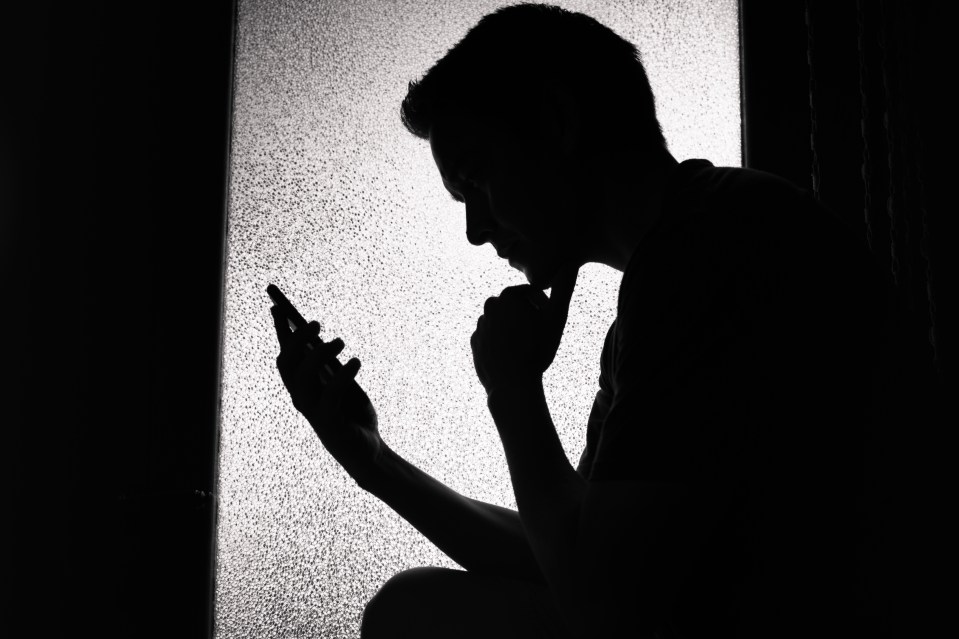 Teenage boy using phone and laptop at night.