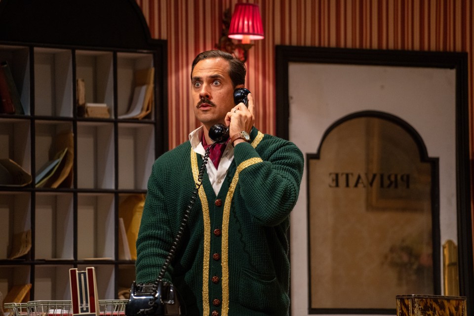 A man in a green cardigan uses a rotary phone.