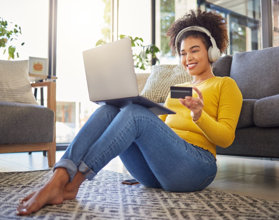 Woman using laptop and credit card while wearing headphones.