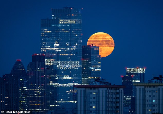 A spectacular full moon rises over The City of London with office lights still burning in some skyscrapers