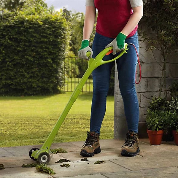 Person using an electric weed sweeper to clear a patio.
