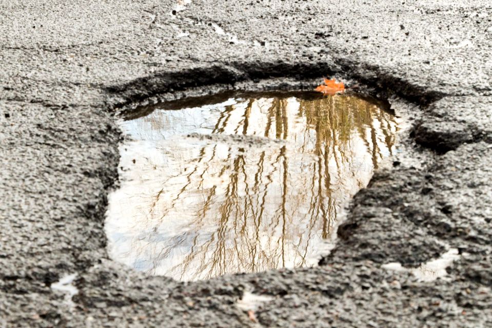 An image collage containing 1 images, Image 1 shows Large pothole in asphalt road reflecting trees