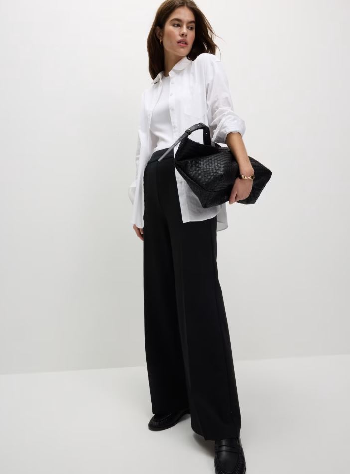 Woman wearing black wide-leg trousers and a white shirt.