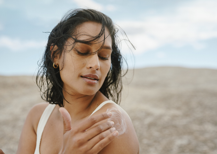 Woman applying sunscreen to her shoulder outdoors.