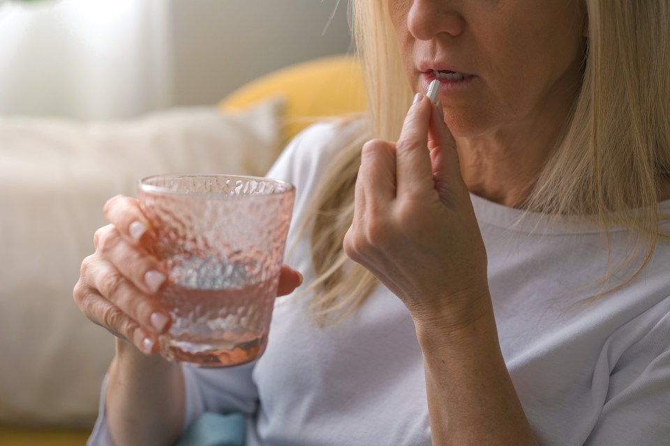 Close-up of a senior woman taking a pill with water.