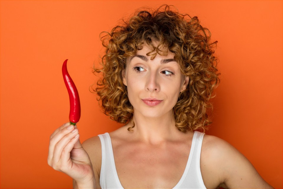 Woman with curly hair holding a chili pepper.