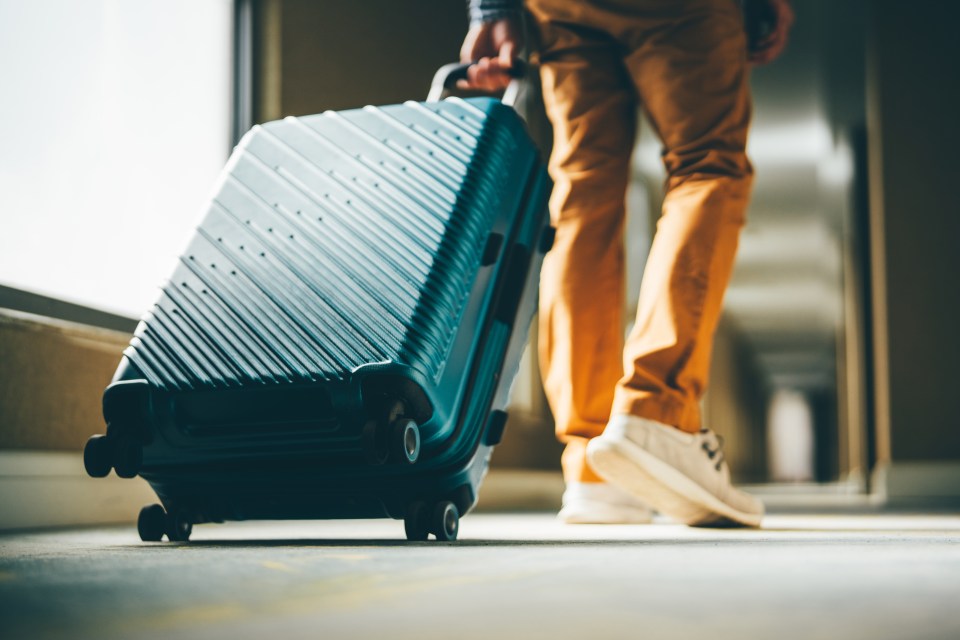 Man pulling wheeled luggage down a hotel corridor.